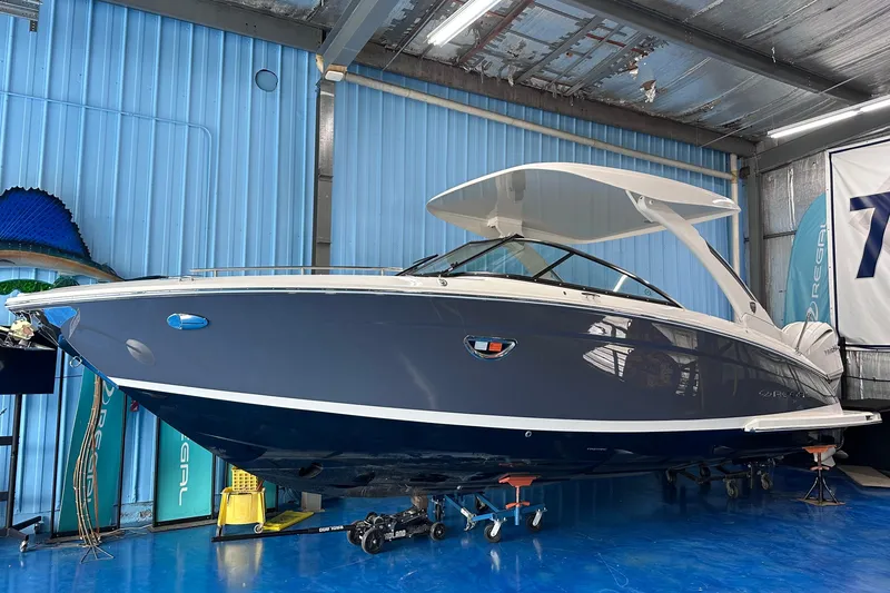 Slide: The Image of 2026 Regal LX9 boat in showroom, sleek design, blue hull, white canopy. - 1