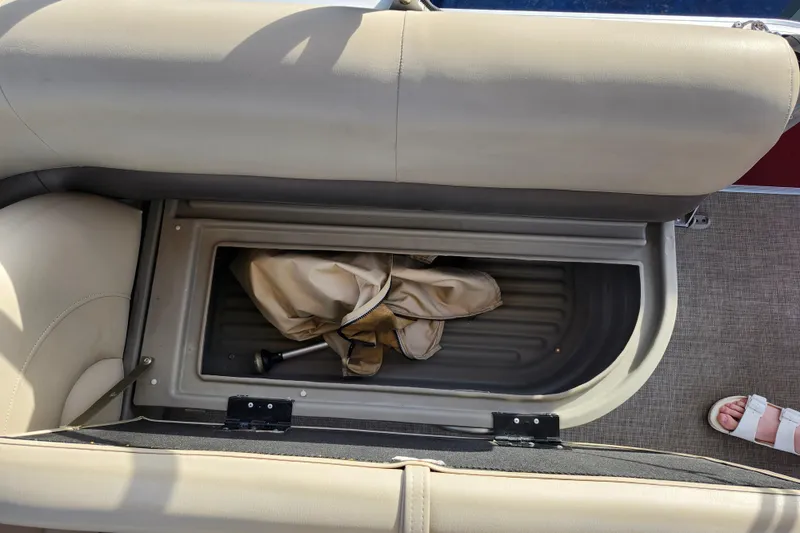 Slide: The Image of 2023 Sun Tracker Bass Buggy 18 DLX storage compartment with beige upholstery and folded cover. - 18