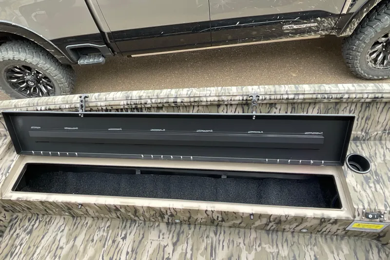 Slide: The Image of Open storage compartment in 2026 Excel Tomahawk 183 boat, camo design, parked beside a truck. - 10