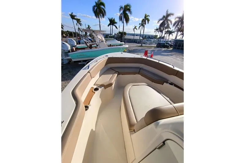 Slide: The Image of 2024 Scout 215 XSF boat interior with tan seating, parked outdoors under palm trees. - 18