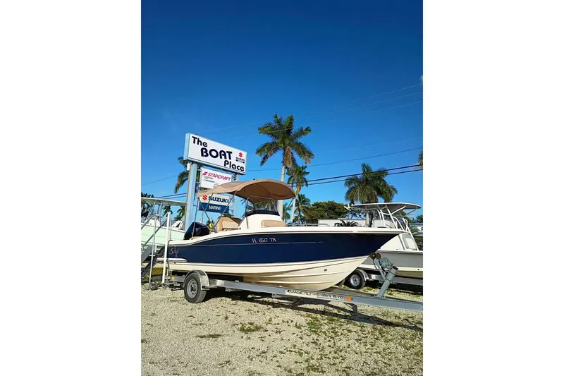 Slide: The Image of 2024 Scout 215 XSF boat on trailer at dealership, palm trees in background. - 2