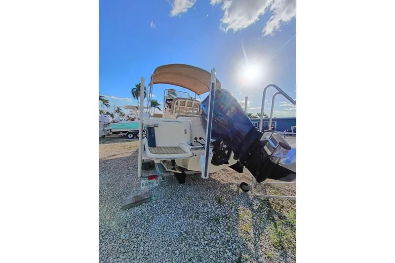 Slide: The Image of 2024 Scout 215 XSF boat with outboard motor, parked on gravel under a sunny sky. - 5