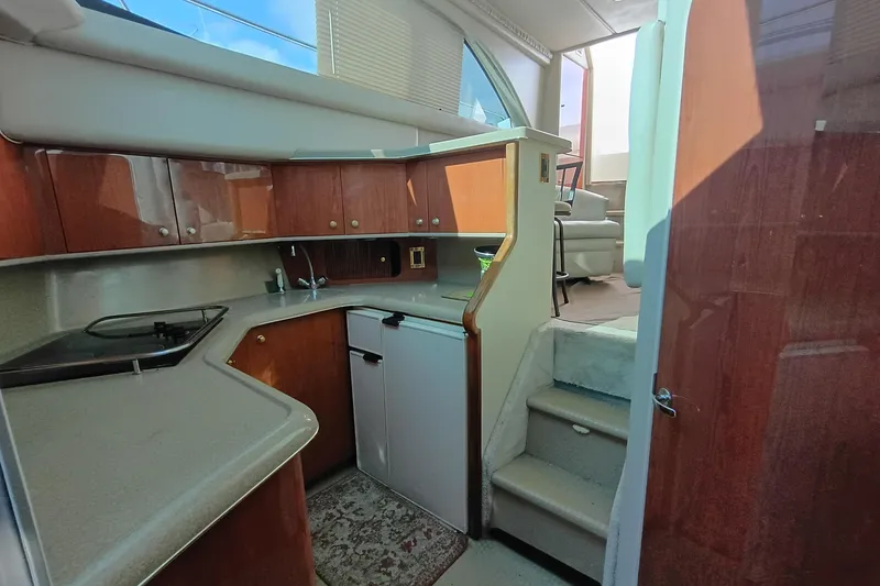 Slide: The Image of 1997 Sea Ray 370 Aft Cabin interior with kitchenette and stairs, featuring wood cabinetry. - 76
