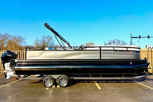 The Image of 2025 Regency 250 DL3 pontoon boat on trailer in parking lot, clear blue sky. - 0