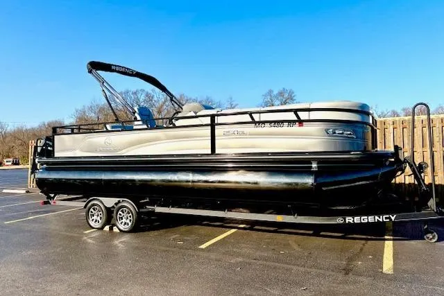 Slide: The Image of 2025 Regency 250 DL3 pontoon boat on trailer in parking lot, clear blue sky. - 2