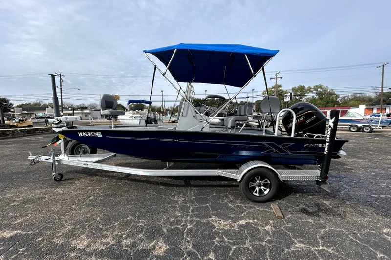 Slide: The Image of 2025 Xpress H20B Bay boat with blue canopy on trailer in parking lot. - 10