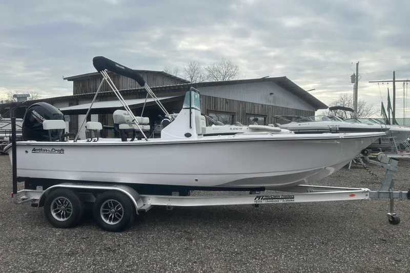 Slide: The Image of 2026 Action Craft 22 Bay boat on trailer, parked outdoors near a wooden building. - 10