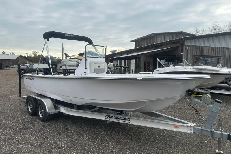 Slide: The Image of 2026 Action Craft 22 Bay boat on trailer, parked outdoors near wooden buildings. - 11