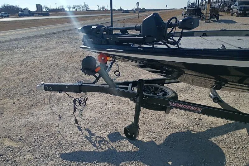 Slide: The Image of 2026 Phoenix 921 Elite X boat trailer on gravel road, featuring hitch and wheel. - 7