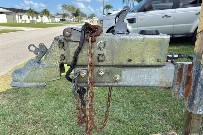 Slide: The Image of Trailer hitch with rusted chain on grass, near a parked car. - 49