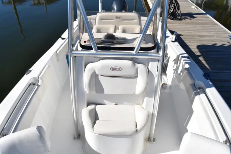 Slide: The Image of 2018 Sea Hunt Ultra 225 boat interior with white seating and console, docked by the water. - 20
