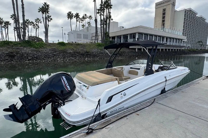 Slide: The Image of 2022 Bayliner VR6 Bowrider OB docked near a hotel, with palm trees in the background. - 2
