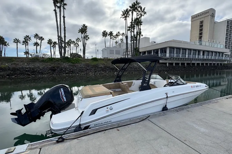 Slide: The Image of 2022 Bayliner VR6 Bowrider OB docked by a waterfront with palm trees and hotel. - 3