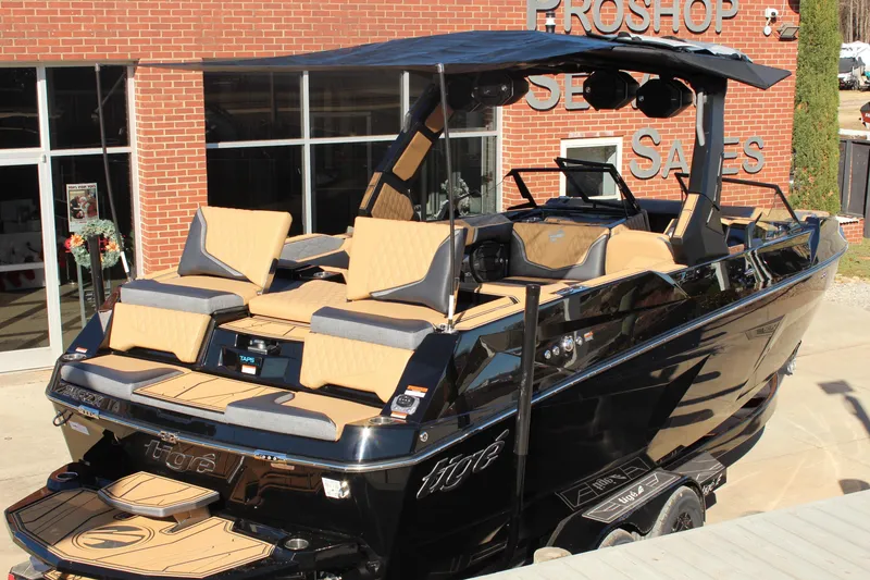 Slide: The Image of 2026 Tigé 24RZX boat with tan seating, black exterior, and canopy, displayed outside a sales shop. - 8