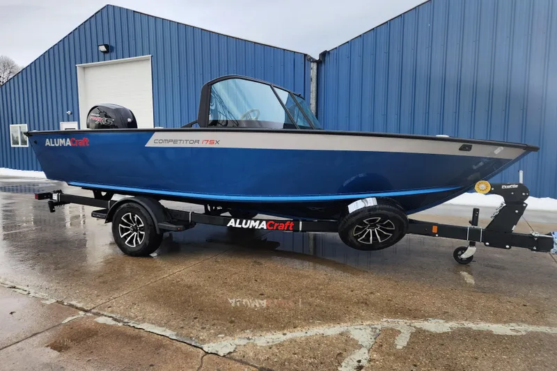 The Image of 2026 Alumacraft Competitor 175 Sport boat on trailer, blue exterior, parked outside blue building. - 1