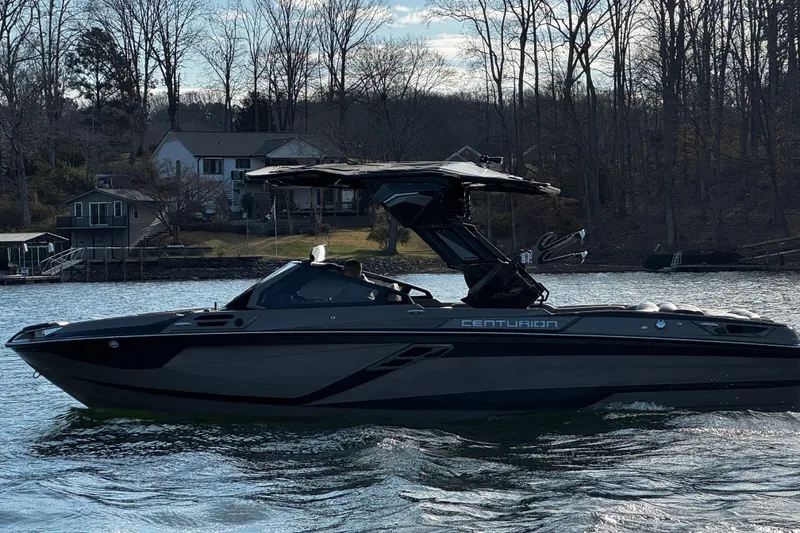 Slide: The Image of 2025 Centurion Ri245 boat on a lake with houses and trees in the background. - 2