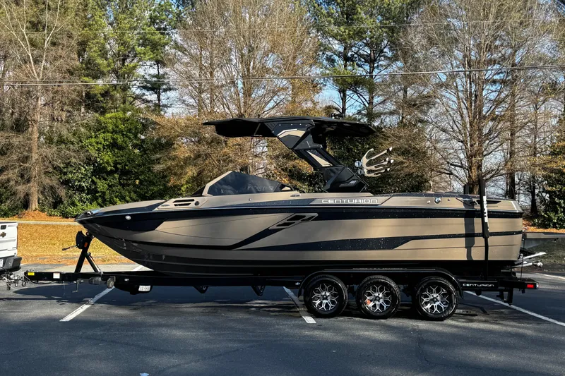 Slide: The Image of 2025 Centurion Ri245 boat on trailer in parking lot, surrounded by trees. - 21