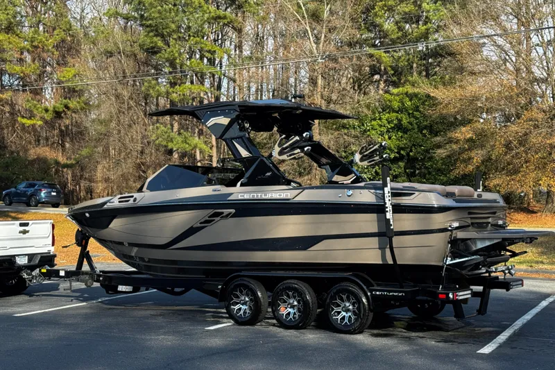 Slide: The Image of 2025 Centurion Ri245 boat on trailer in parking lot, surrounded by trees. - 22