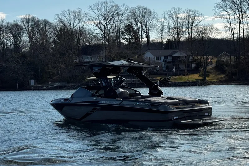 Slide: The Image of 2025 Centurion Ri245 boat cruising on a lake with a scenic shoreline backdrop. - 4