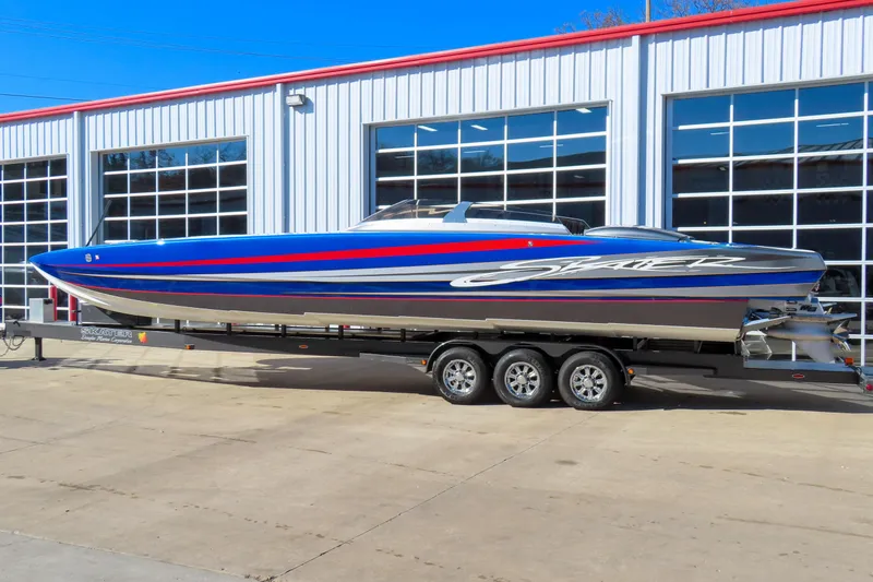 The Image of 2016 Skater 388 powerboat on trailer, blue and red design, parked outside a garage. - 1