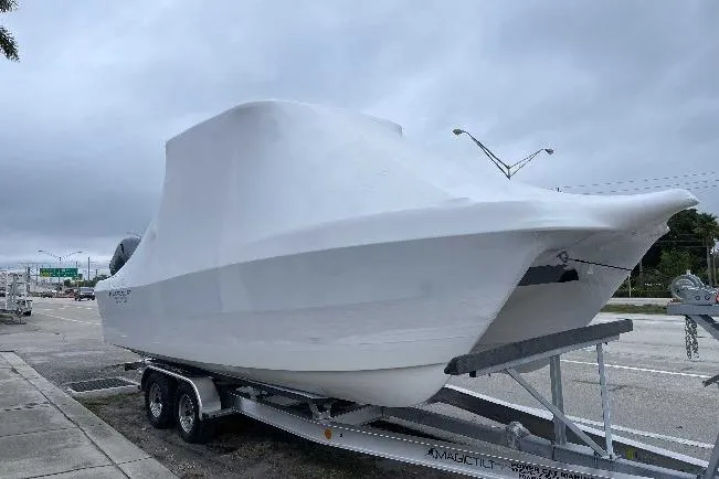 The Image of 2025 World Cat 230 DC boat covered on trailer, parked outdoors under cloudy sky. - 0
