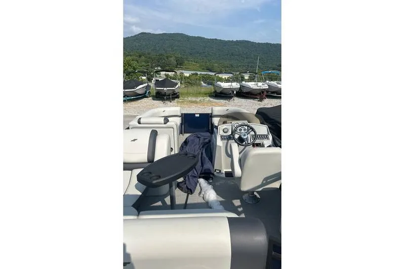 Slide: The Image of 2024 Starcraft EXS 3 Q boat interior with steering wheel and seating, parked near mountains. - 6