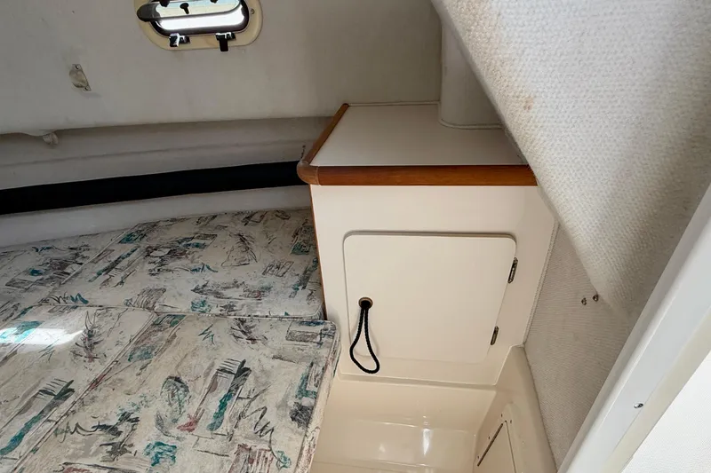 Slide: The Image of 1999 Pursuit 2470 Walkaround cabin interior with patterned cushions and storage compartment. - 27