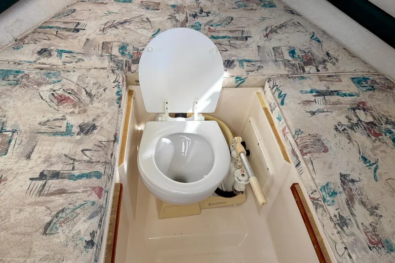 Slide: The Image of 1999 Pursuit 2470 Walkaround boat interior with marine toilet and patterned cushions. - 30