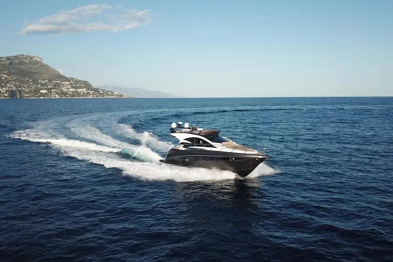 Slide: The Image of 2025 Cobrey 52 FLY yacht cruising on open sea with scenic coastal backdrop. - 5