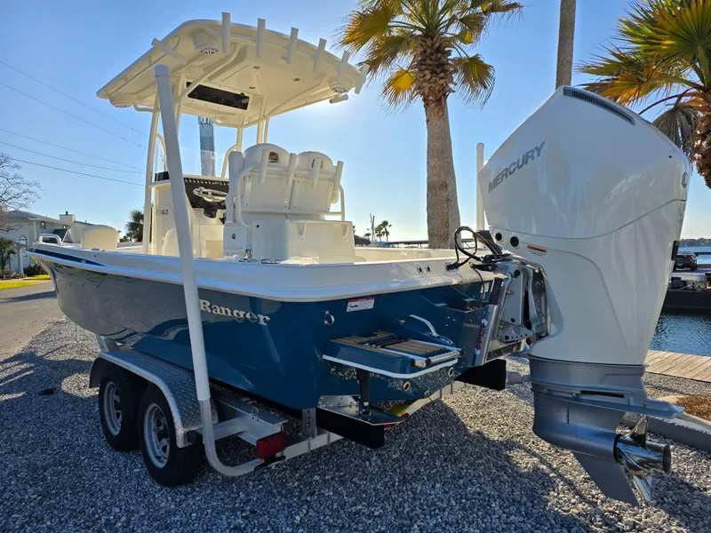 Slide: The Image of 2025 Ranger 2360 Bay boat with Mercury engine on trailer, parked near palm trees. - 2