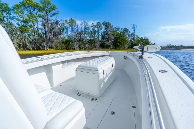 Slide: The Image of 2014 Yellowfin 32 Offshore boat interior with white seating, near lush shoreline. - 14