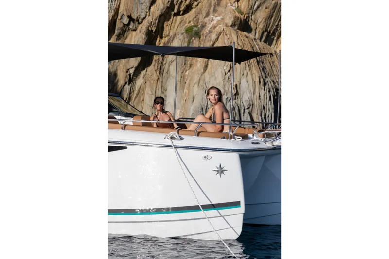 Slide: The Image of 2026 Jeanneau TH33 boat with two people relaxing, anchored near rocky cliffs. - 11