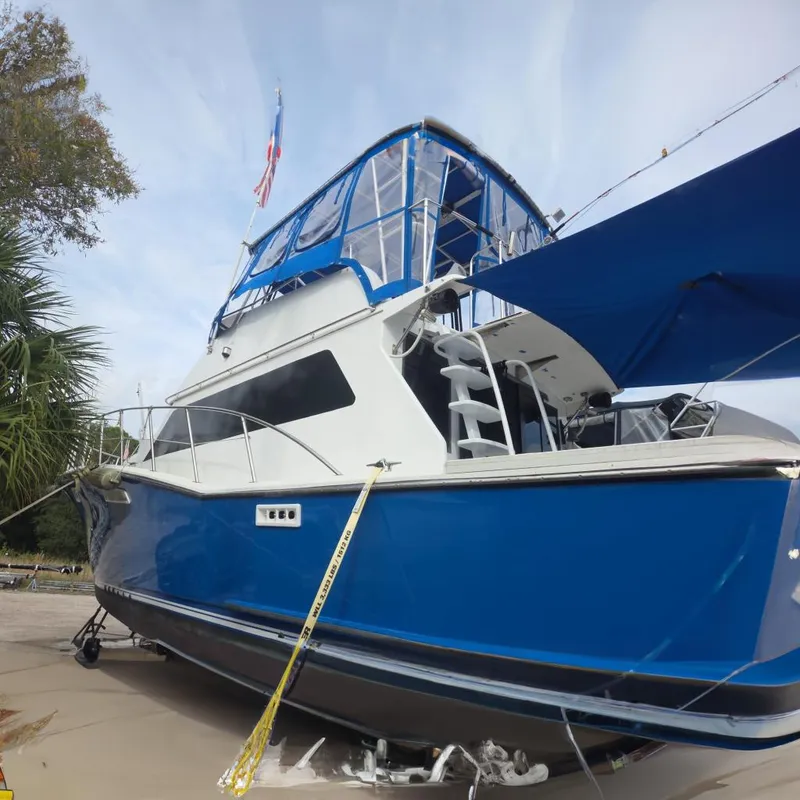 The Image of 1988 Symbol 44' Sportfish boat with blue and white design, docked near lush greenery. - 0