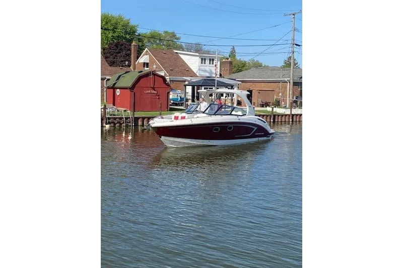 The Image of 2013 Chaparral 327 SSX boat cruising on a calm river near houses. - 0