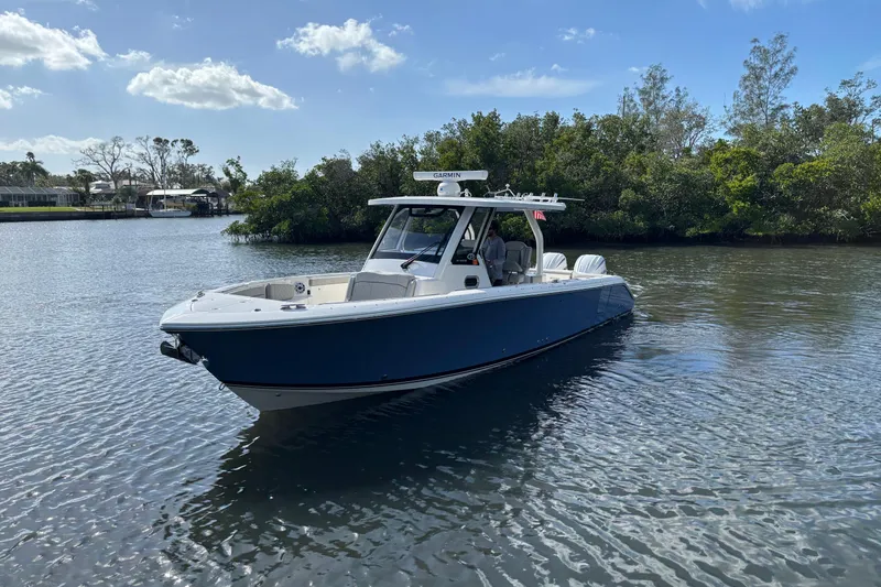 Slide: The Image of 2023 Pursuit S 328 Sport boat on calm water, surrounded by lush greenery. - 3