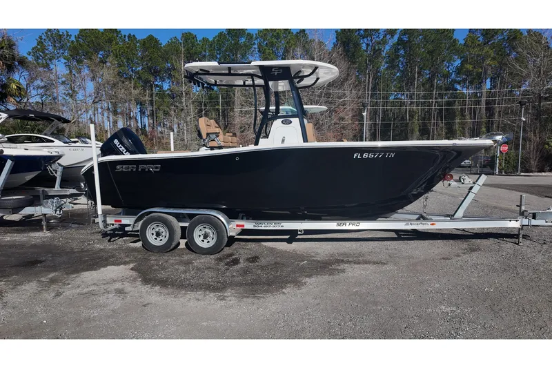 Slide: The Image of 2023 Sea Pro boat on trailer, parked outdoors with trees in background. - 2