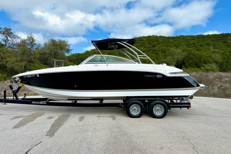 Slide: The Image of 2011 Cobalt 276 boat on trailer, parked outdoors with scenic background. - 10