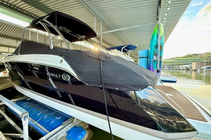 Slide: The Image of 2011 Cobalt 276 boat docked under a covered marina with kayaks nearby. - 17