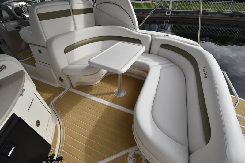 Slide: The Image of 2006 Sea Ray 320 Sundancer interior with white seating and table, docked by water. - 6
