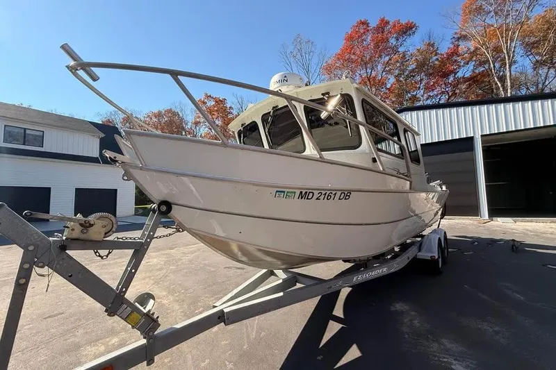 Slide: The Image of 2004 Boulton Explorer 24 boat on trailer, parked near buildings with autumn trees. - 2