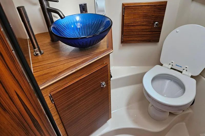 Slide: The Image of Luxurious 2025 Ranger Tugs R-27 bathroom with blue glass sink and wooden cabinetry. - 24