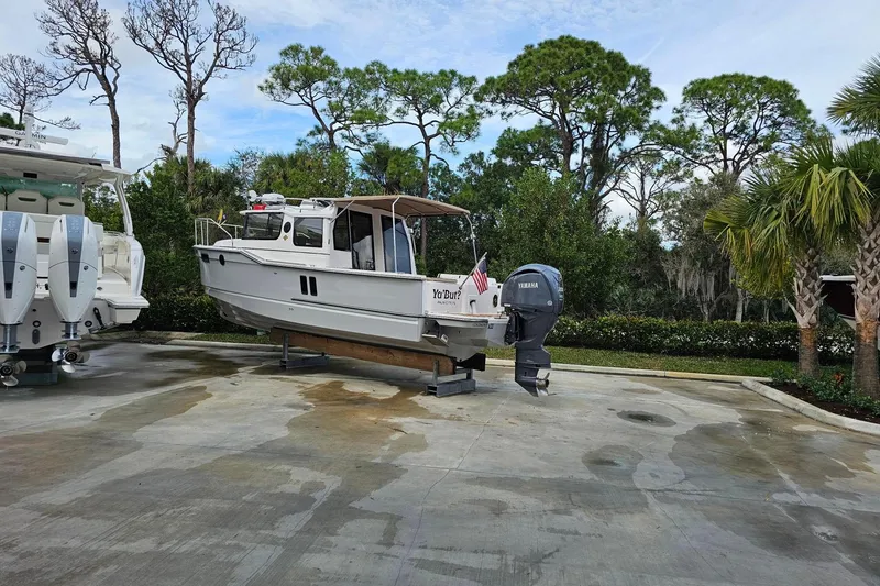 Slide: The Image of 2025 Ranger Tugs R-27 boat on trailer, surrounded by trees and parked on concrete. - 7