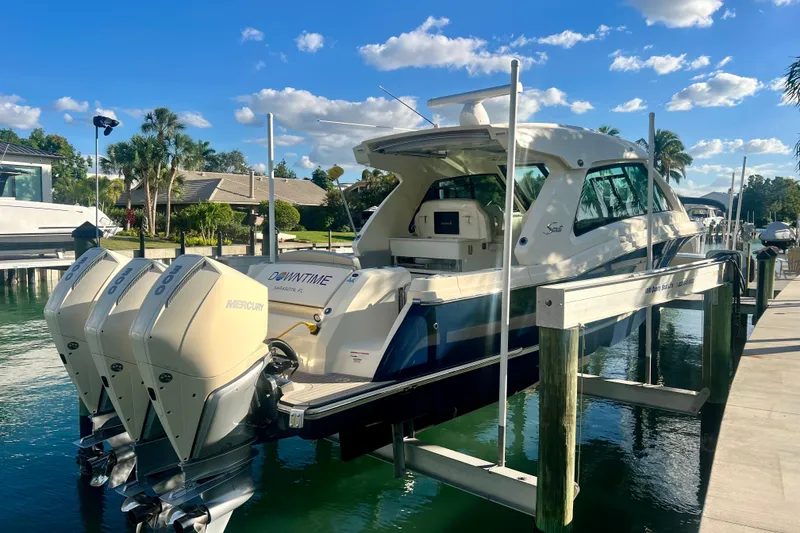 Slide: The Image of 2023 Scout 350 LXZ boat docked with triple Mercury engines, under a clear blue sky. - 2