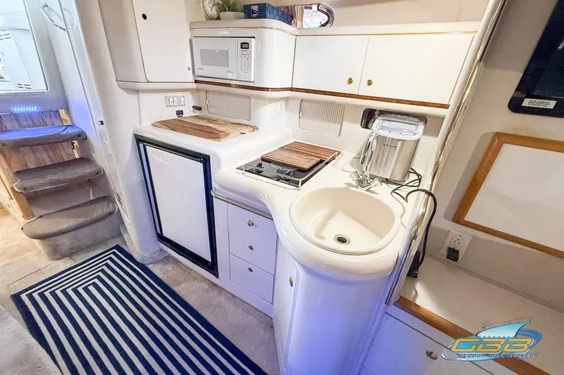 Slide: The Image of 1997 Sea Ray 330 Sundancer kitchen with sink, stove, microwave, and striped rug. - 30