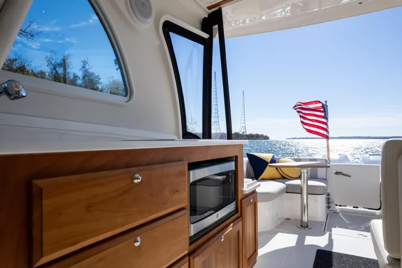 Slide: The Image of 2023 Back Cove 340 interior with kitchenette, seating, and American flag on a sunny day. - 10