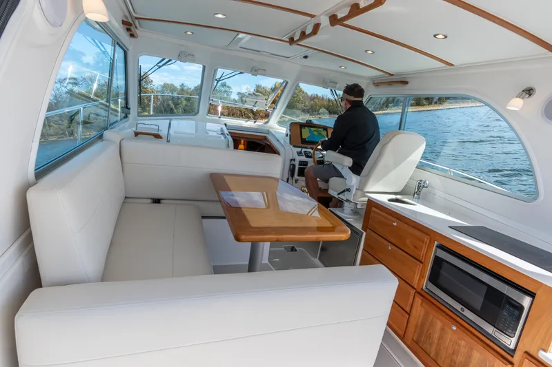 Slide: The Image of 2023 Back Cove 340 interior with helm, seating, and kitchenette on a sunny day. - 16
