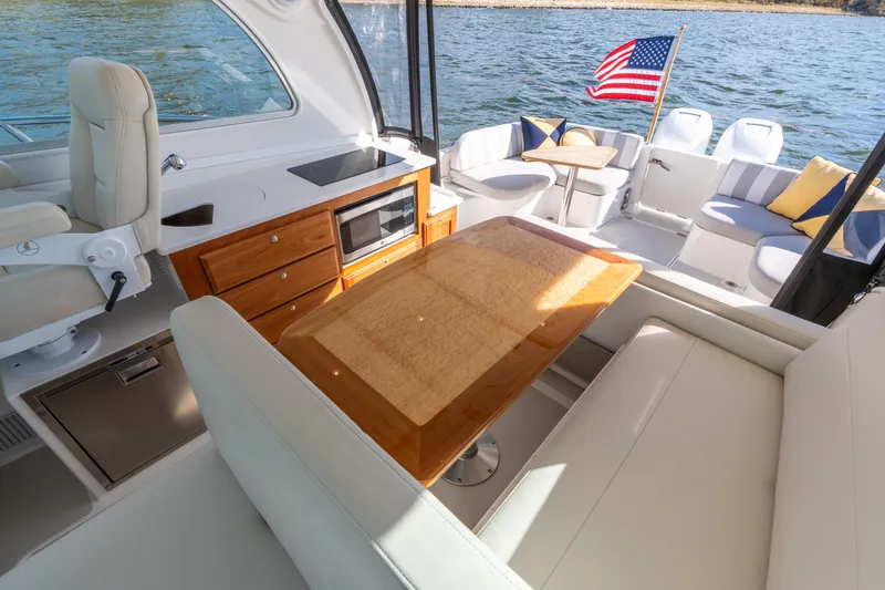 Slide: The Image of 2023 Back Cove 340 boat interior with seating, kitchenette, and American flag on water. - 26