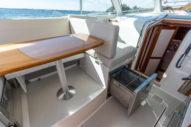 Slide: The Image of 2023 Back Cove 340 interior with seating, table, and open storage drawer, overlooking the water. - 29