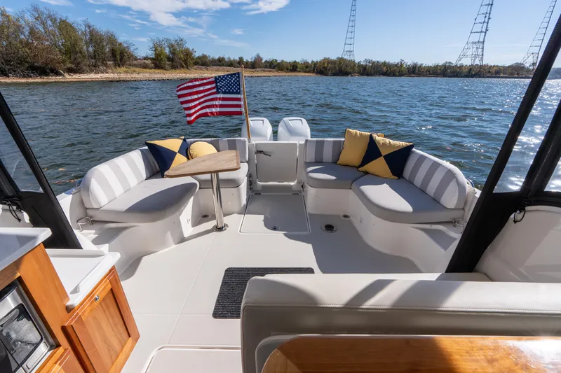 Slide: The Image of 2023 Back Cove 340 boat interior with seating, table, and American flag on a sunny day. - 8