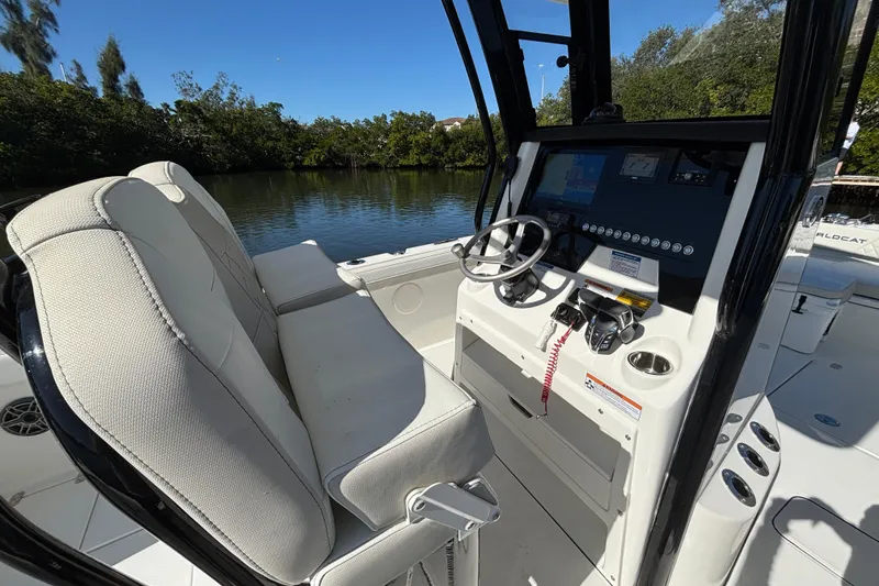 Slide: The Image of 2026 World Cat 235 TE boat interior with steering console and seating, docked by a scenic waterway. - 10